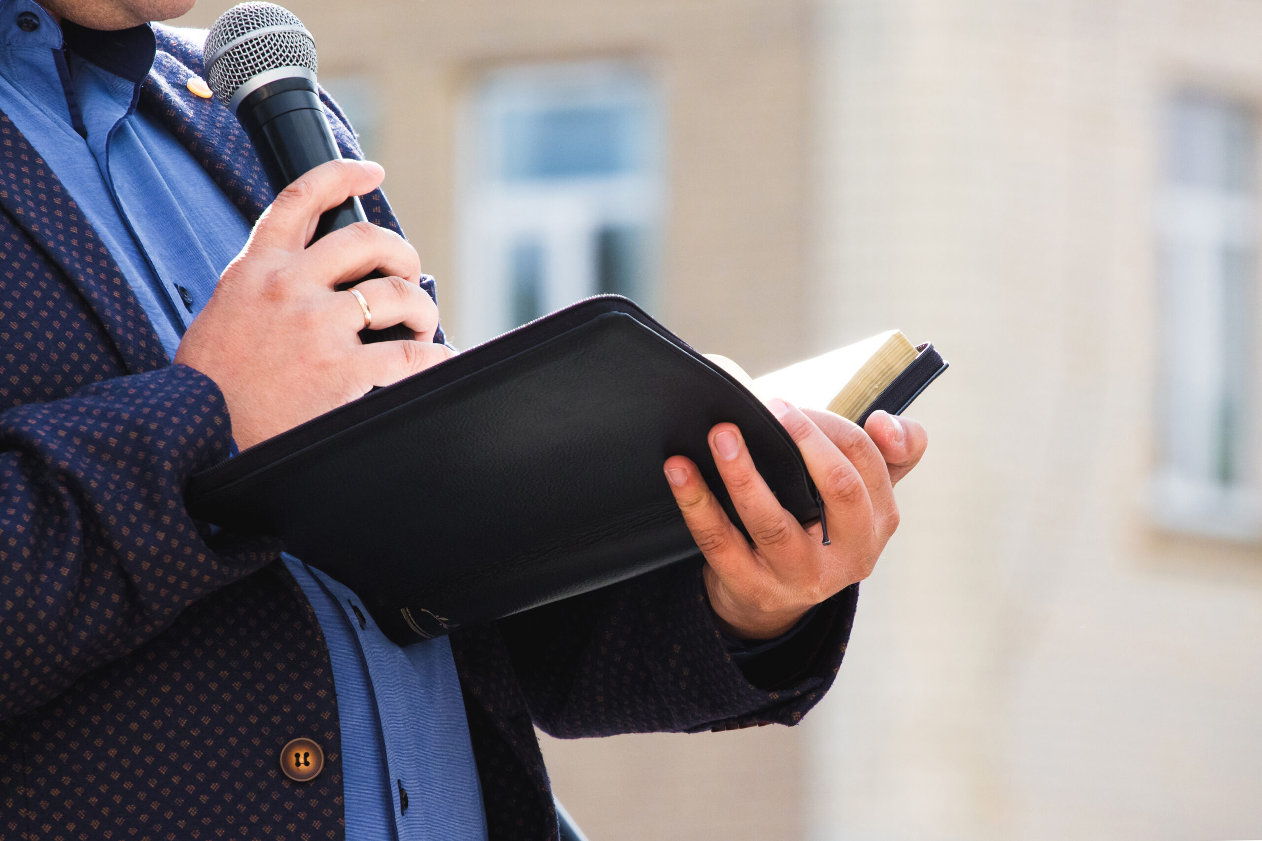 A preacher with a microphone in his hand holds a Bible and reads