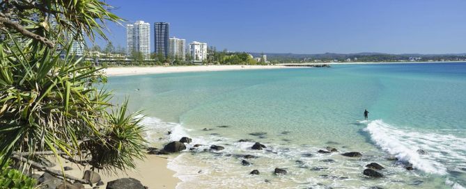 Coolangatta Beach with clear blue water, sandy shoreline and high-rise buildings in the distance.